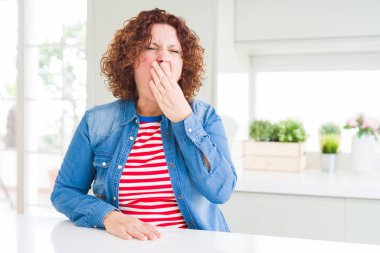Evde kot ceket giyen kıvırcık saçlı orta yaş yaşlı kadın el ile ağız kapsayan yorgun esneme sıkılmış. Huzursuz ve uykululuk.