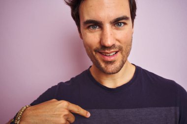 Kendine işaret sürpriz yüzü ile izole pembe arka plan üzerinde duran rahat t-shirt giyen genç yakışıklı adam