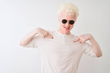 Genç albino sarışın adam izole beyaz arka plan üzerinde t-shirt ve güneş gözlüğü giyen yüzünde gülümseme ile emin görünümlü, parmakları gururlu ve mutlu kendini işaret.