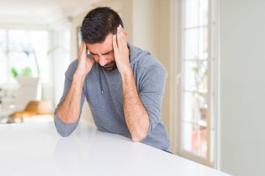 Yakışıklı İspanyol adam evde rahat sweatshirt giyen baş ağrısı umutsuz muzdarip ve stresli çünkü ağrı ve migren. Eller baş üstünde.