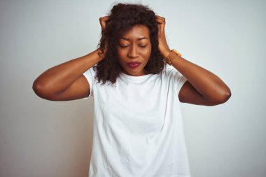Genç afro-amerikan kadın izole beyaz arka plan üzerinde ayakta t-shirt giyen baş ağrısı umutsuz muzdarip ve stresli çünkü ağrı ve migren. Eller baş üstünde.