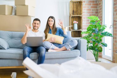 Genç güzel çift parmakları, mükemmel sembolü ile ok işareti yapıyor bilgisayar dizüstü bilgisayar kullanarak yeni evin kanepede oturan rahatlatıcı