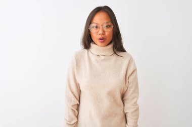 Genç çinli kadın boğazlı kazak ve gözlük izole beyaz arka plan üzerinde korkmuş ve sürpriz ifade, korku ve heyecanlı yüz ile şok giyen.