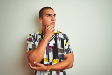 Genç yakışıklı adam soru, dalgın ifade hakkında düşünme çene üzerinde el ile beyaz izole arka plan üzerinde yazlık gömlek giyiyor. Düşünceli bir yüzle gülümsüyor. Şüphe kavramı.