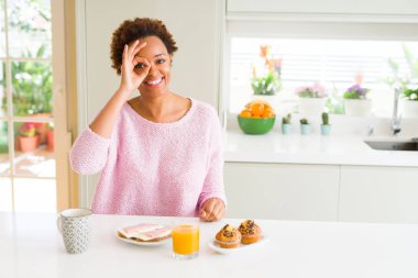 Genç afro-amerikan kadın evde sabah breaksfast yeme el gülümseyerek ok jest yapıyor, mutlu yüz ile parmaklarından bakan göz.