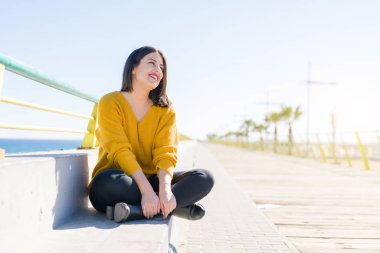 Güzel genç kadın bir mesire neşeli zevk güneş ışığı güneşli günde rahatlatıcı gülümseyen deniz kenarında oturup...