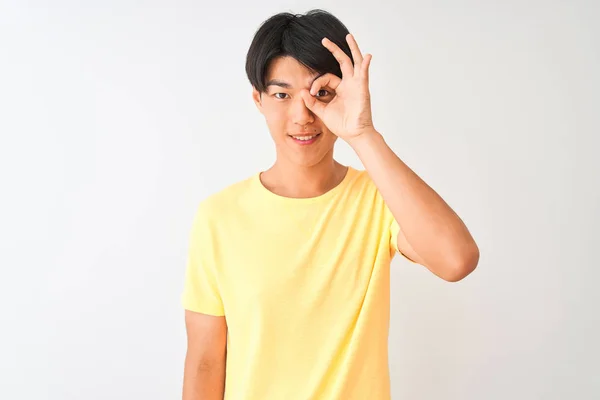 孤立した白い背景の上に立つ黄色のカジュアルなTシャツを着た中国人男性は 笑顔でOkジェスチャーを行い 幸せそうな顔で指を通して目を見る — ストック写真