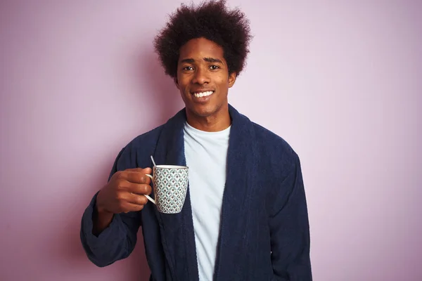 Afro american man wearing pajama drinking coffee standing over isolated pink background with a happy face standing and smiling with a confident smile showing teeth