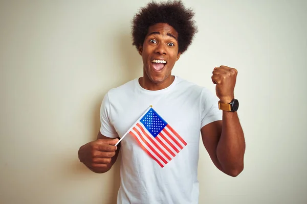 Afro man holding United Estates of America USA flag standing over isolated white background screaming proud and celebrating victory and success very excited, cheering emotion