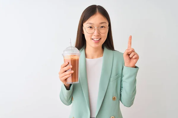 年轻的中国妇女喝番茄冰沙在孤立的白色背景惊讶与一个想法或问题指向手指与快乐的脸 — 图库照片