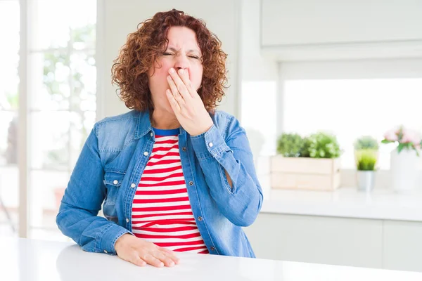 Evde kot ceket giyen kıvırcık saçlı orta yaş yaşlı kadın el ile ağız kapsayan yorgun esneme sıkılmış. Huzursuz ve uykululuk.