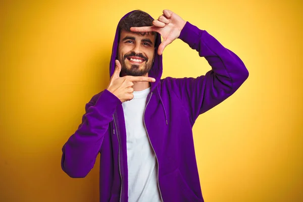 有纹身的年轻人穿着紫色运动衫 头罩在孤立的黄色背景微笑 用手和手指与快乐的脸框 创意与摄影理念 — 图库照片