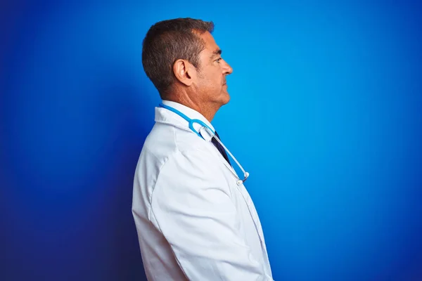 Handsome middle age doctor man wearing stethoscope over isolated blue background looking to side, relax profile pose with natural face with confident smile.