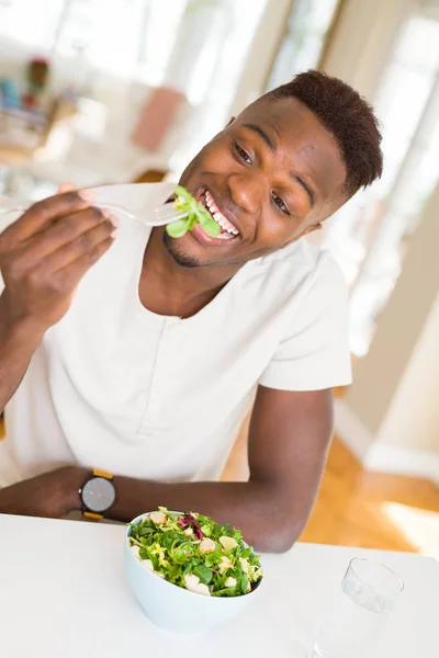 レタス 幸せと笑顔のテーブルに座っての食べ方 フォークを使用してヘルシーな野菜サラダを食べるアフリカ若い美男子 — ストック写真