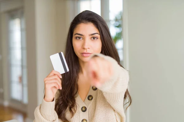 Young woman holding credit card as payment pointing with finger to the camera and to you, hand sign, positive and confident gesture from the front