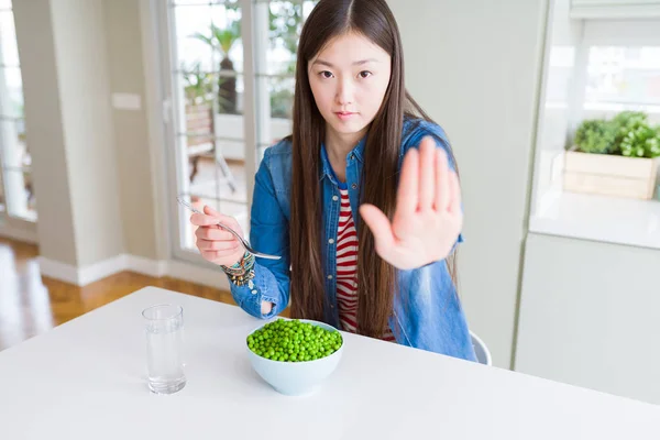 真面目で自信に満ちた表情でストップサインをするオープンハンドで新鮮な緑のエンドウ豆を食べる美しいアジアの女性 防衛ジェスチャー — ストック写真