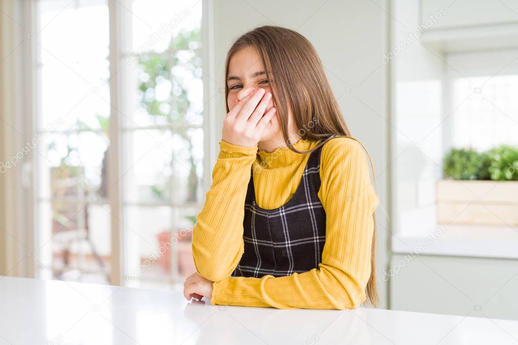 Young beautiful blonde kid girl wearing casual yellow sweater at home smelling something stinky and disgusting, intolerable smell, holding breath with fingers on nose. Bad smells concept.