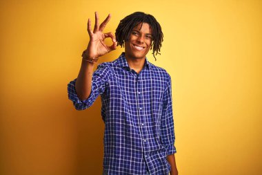 Yalnız sarı arka plan üzerinde duran rahat gömlek giyen dreadlocks ile Afro adam el ve parmakları ile ok işareti yapıyor olumlu gülümseyerek. Başarılı ifade.