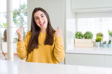 Beautiful young woman wearing yellow sweater celebrating surprised and amazed for success with arms raised and open eyes. Winner concept.