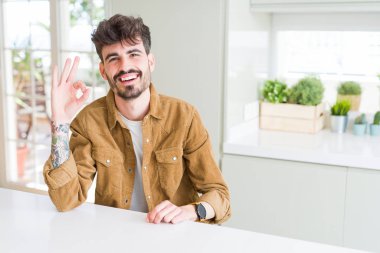 Beyaz masada oturan rahat ceket giyen genç adam el ve parmakları ile ok işareti yapıyor olumlu gülümseyerek. Başarılı ifade.
