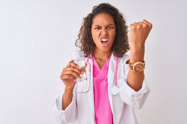 Genç Brezilyalı doktor kadın izole beyaz arka plan üzerinde duran su bardağı tutan rahatsız ve öfke ile bağırarak sinirli, deli ve yükseltilmiş el ile bağırıyor, öfke kavramı