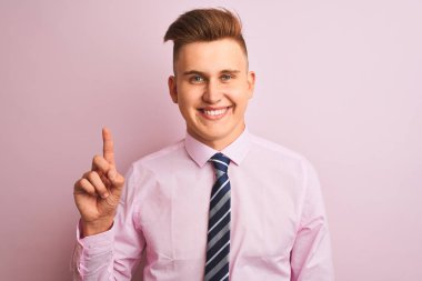 Genç yakışıklı işadamı gömlek ve kravat izole pembe arka plan üzerinde duran gösteren ve kendinden emin ve mutlu gülümserken parmak sayısı bir işaret.