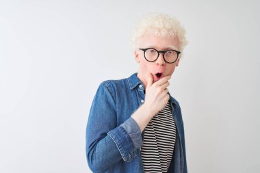 Genç albino sarışın adam izole beyaz arka plan üzerinde denim gömlek ve gözlük giyen güvensizlik, sürpriz ve çene elleri ile hayran ifade hayran arıyorum