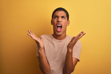 Genç yakışıklı Arap adam çizgili t-shirt izole sarı arka plan deli ve deli bağırarak ve agresif ifade ve kollar kaldırdı ile bağırarak üzerinde duran giyiyor. Hayal kırıklığı kavramı.