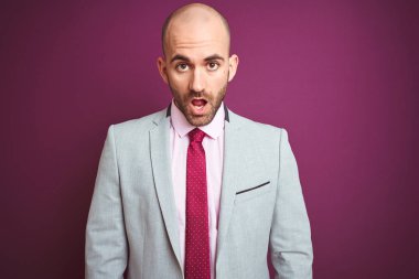 Mor izole arka plan üzerinde takım elbise ve kravat giyen genç iş adamı korkmuş ve sürpriz ifade, korku ve heyecanlı yüz ile şok.