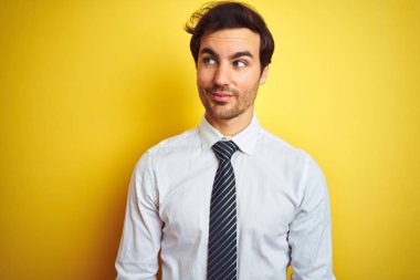 Genç yakışıklı işadamı izole sarı arka plan üzerinde zarif gömlek ve kravat giyen yan bakarak gülümseyerek ve düşünme uzak bakıyor.