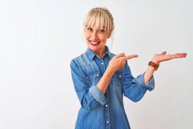 Izole beyaz arka plan üzerinde duran rahat kot gömlek giyen orta yaş kadın şaşırttı ve el ile sunarken kameraya gülümseyerek ve parmak ile işaret.