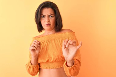 Izole turuncu arka plan üzerinde duran rahat t-shirt giyen genç güzel kadın tiksinti ifade, hoşnutsuz ve korkulu tiksinti yüz yapıyor çünkü nefret tepki. Elleri havada. Sinir bozucu kavram.