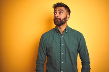 İzole beyaz arka plan üzerinde duran zarif gömlek giyen genç Hintli işadamı yan bakarak gülümseyerek ve düşünme uzak bakıyor.