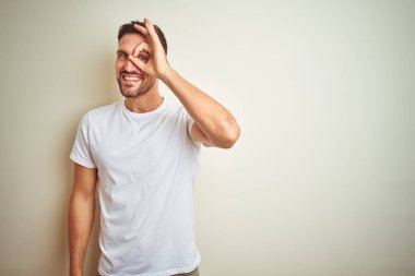 Gülümseyen, parmakları ile mutlu yüz üzerinden seyir göz el ile ok jest yapıyor izole arka plan üzerinde rahat beyaz t-shirt giyen genç yakışıklı adam.