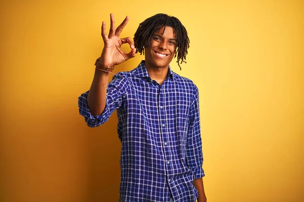 Yalnız sarı arka plan üzerinde duran rahat gömlek giyen dreadlocks ile Afro adam el ve parmakları ile ok işareti yapıyor olumlu gülümseyerek. Başarılı ifade.