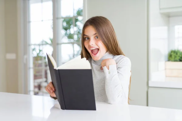 Beautiful Young Girl Reading Book Home Surprise Face Pointing Finger — Stock Photo, Image