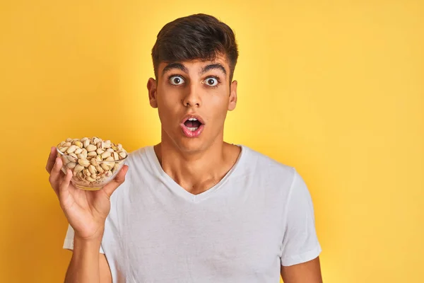 Young Indian Man Holding Bowl Pistachios Isolated Yellow Background Scared — Stock Photo, Image