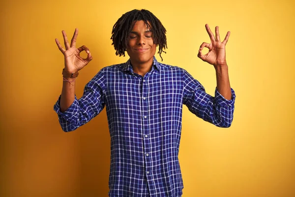 Izole sarı arka plan üzerinde duran rahat gömlek giyen dreadlocks ile Afro adam rahat ve gözleri parmakları ile meditasyon jest yapıyor kapalı gülümseyerek. Yoga konsepti.