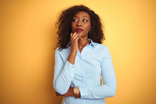 African american businesswoman wearing elegant shirt over isolated yellow background with hand on chin thinking about question, pensive expression. Smiling with thoughtful face. Doubt concept.