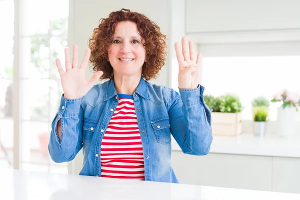 Kıvırcık saçlı orta yaş yaşlı kadın evde kot ceket giyen gösteren ve parmakları ile işaret ederken emin ve mutlu gülümsüyor.