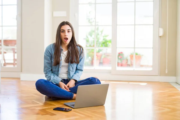 美丽的年轻女子坐在地板上 交叉的双腿使用笔记本电脑害怕和震惊与惊喜的表情 恐惧和兴奋的脸 — 图库照片