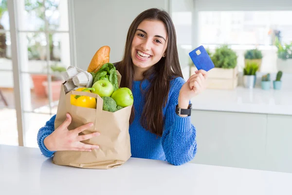 Mujer joven sosteniendo una bolsa de papel llena de alimentos frescos y mostrar — Foto de Stock