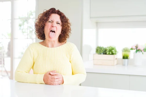 黄色いセーターを着た美しい先輩女性がおかしな表情で舌を突き出す 感情の概念 — ストック写真