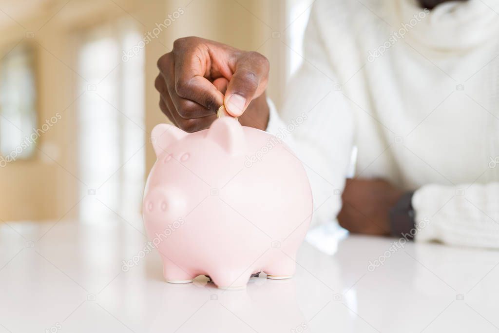 Close up of african man hands putting a coin inside piggy bank, saving money as investment