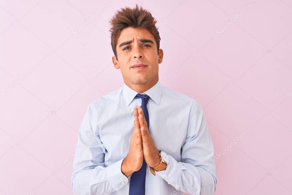 Young handsome businessman wearing shirt and tie standing over isolated pink background begging and praying with hands together with hope expression on face very emotional and worried. Asking for forgiveness. Religion concept.