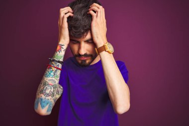 Dövmeli genç adam izole mor arka plan üzerinde ayakta t-shirt giyen baş ağrısı umutsuz muzdarip ve stresli çünkü ağrı ve migren. Eller baş üstünde.