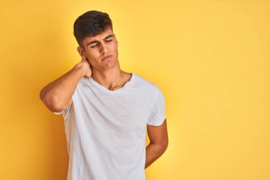 İzole sarı arka plan üzerinde duran beyaz t-shirt giyen genç hintli adam boyun ağrısı yaralanma, el ile boyun dokunmadan, kas ağrısı