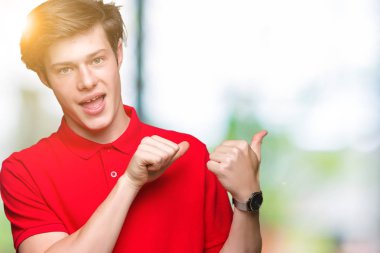 Üzerinde kırmızı t-shirt giyen genç yakışıklı adam izole arka plan emin gülümseyen arkasından el ve kadar başparmak ile işaret