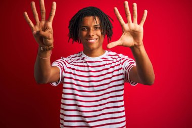 Kendinden emin ve mutlu gülümserken izole kırmızı arka plan üzerinde duran çizgili t-shirt giyen dreadlocks ile genç afro adam gösteren ve parmakları sayısı dokuz ile işaret.