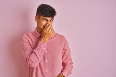 İzole pembe arka plan üzerinde duran zarif gömlek giyen genç hintli adam, kokuşmuş ve, dayanılmaz bir koku kokuyor, burnunda parmaklarıyla nefes tutuyor. Kötü kokular kavramı.